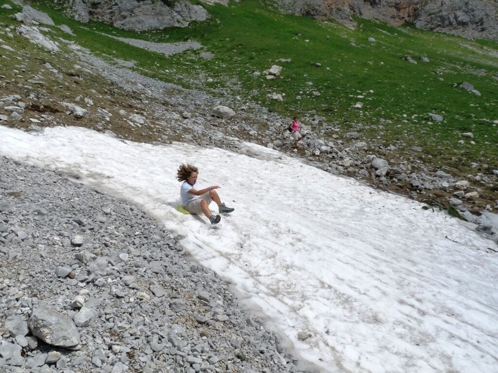 A person sitting on a snow-covered slope with rocky terrain and sparse vegetation in the background.