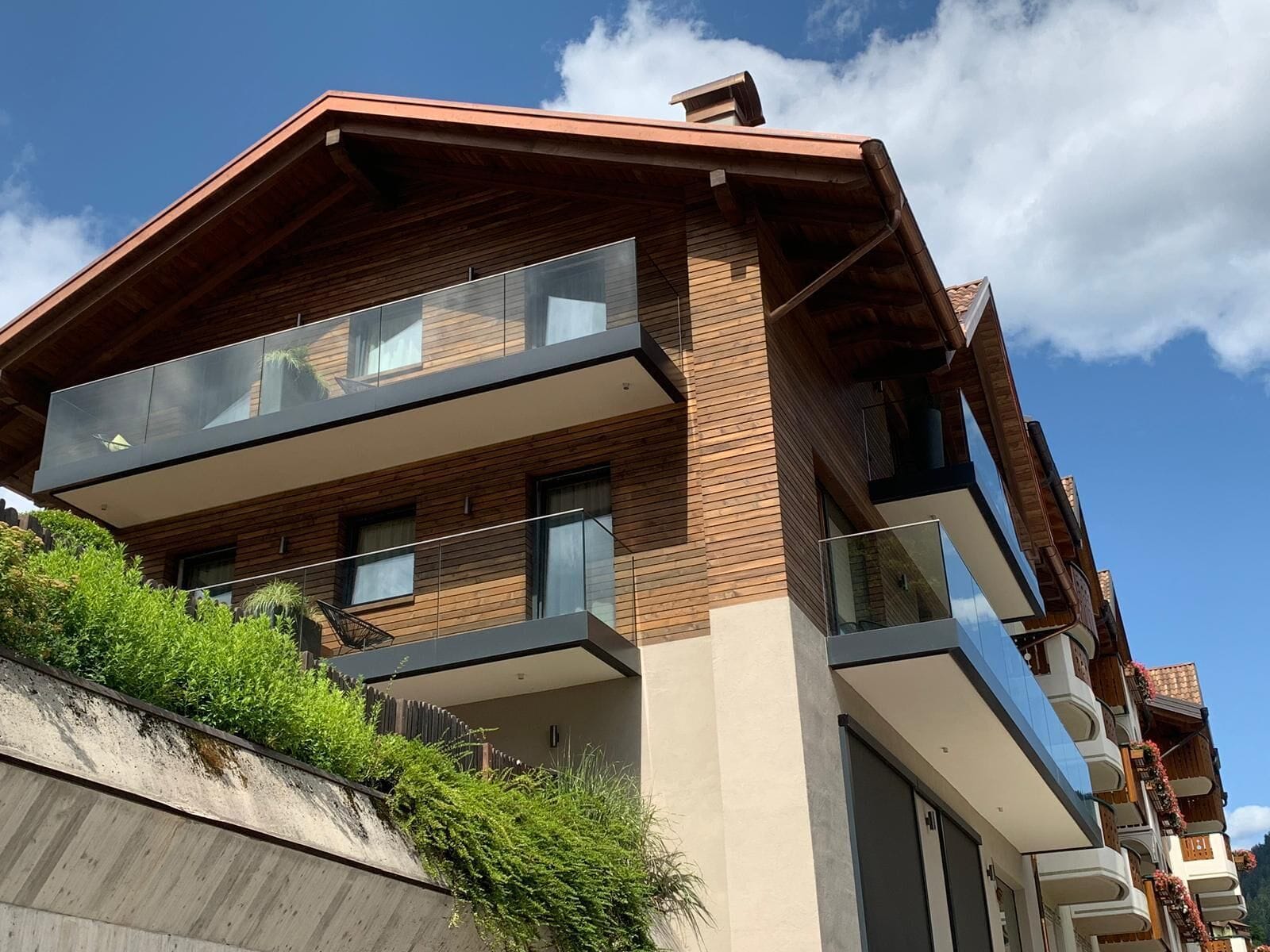 Ein modernes, mehrgeschossiges Gebäude mit Holzfassade, großen Fenstern und Balkonen.