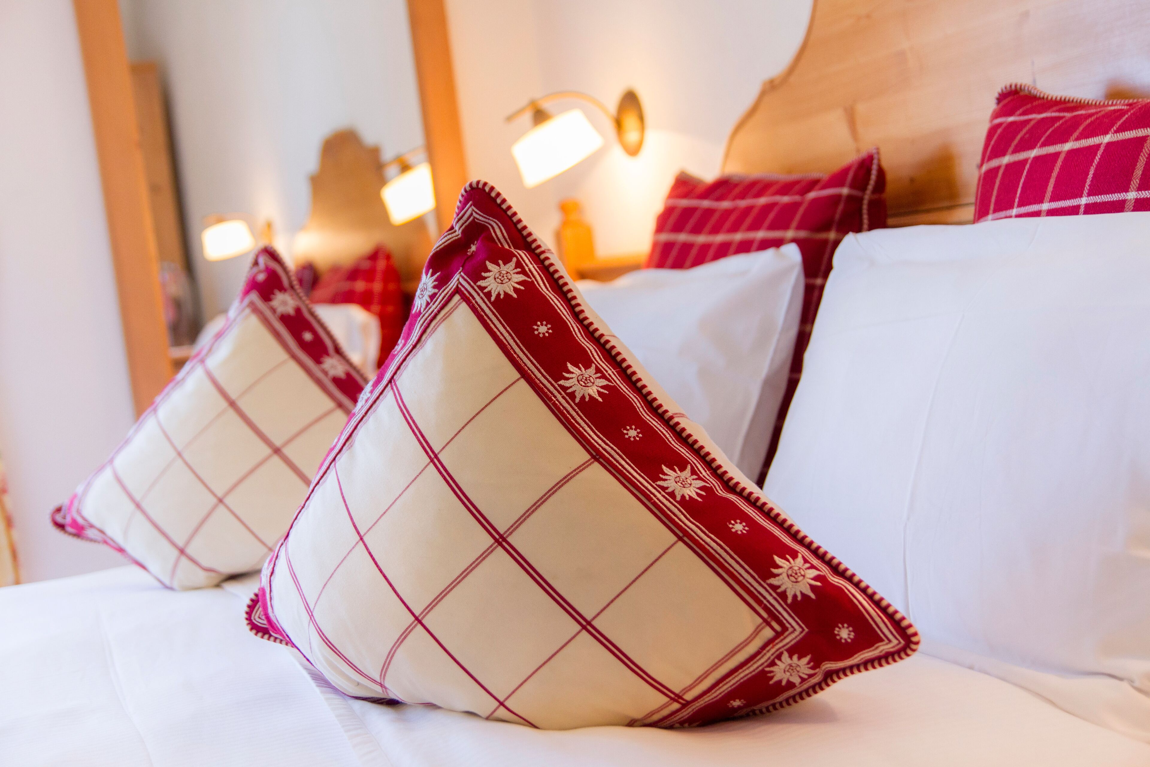 Una cama con ropa blanca y almohadas estampadas en rojo y blanco.