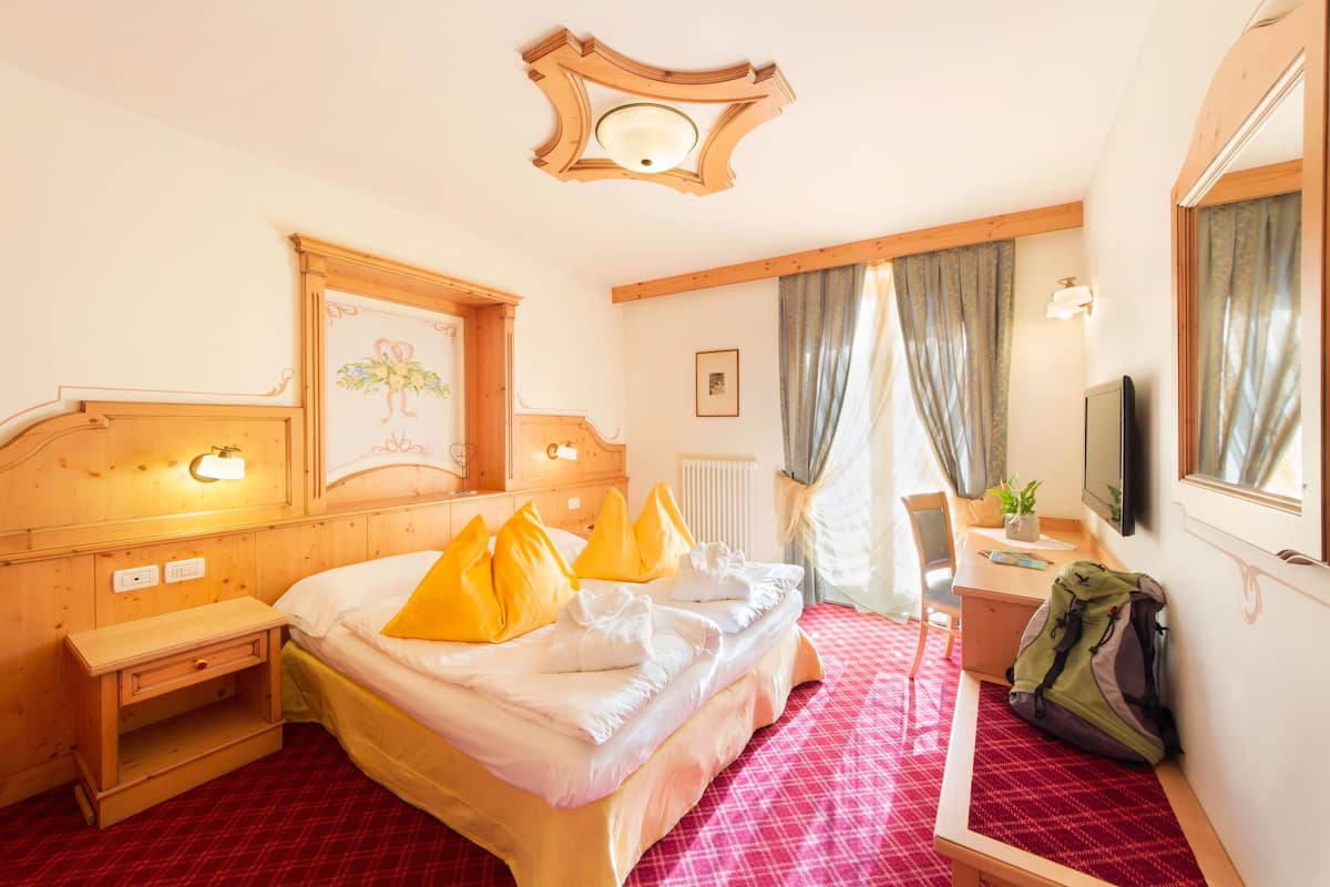 A hotel room with a bed, bedside table, desk, chair, and a window with curtains.