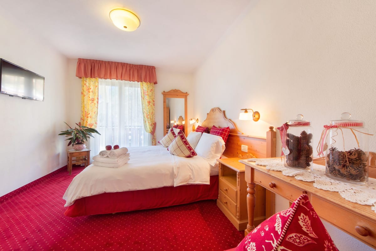 A hotel room with a large bed, a wooden nightstand, a mirror, and a desk with decorative jars.