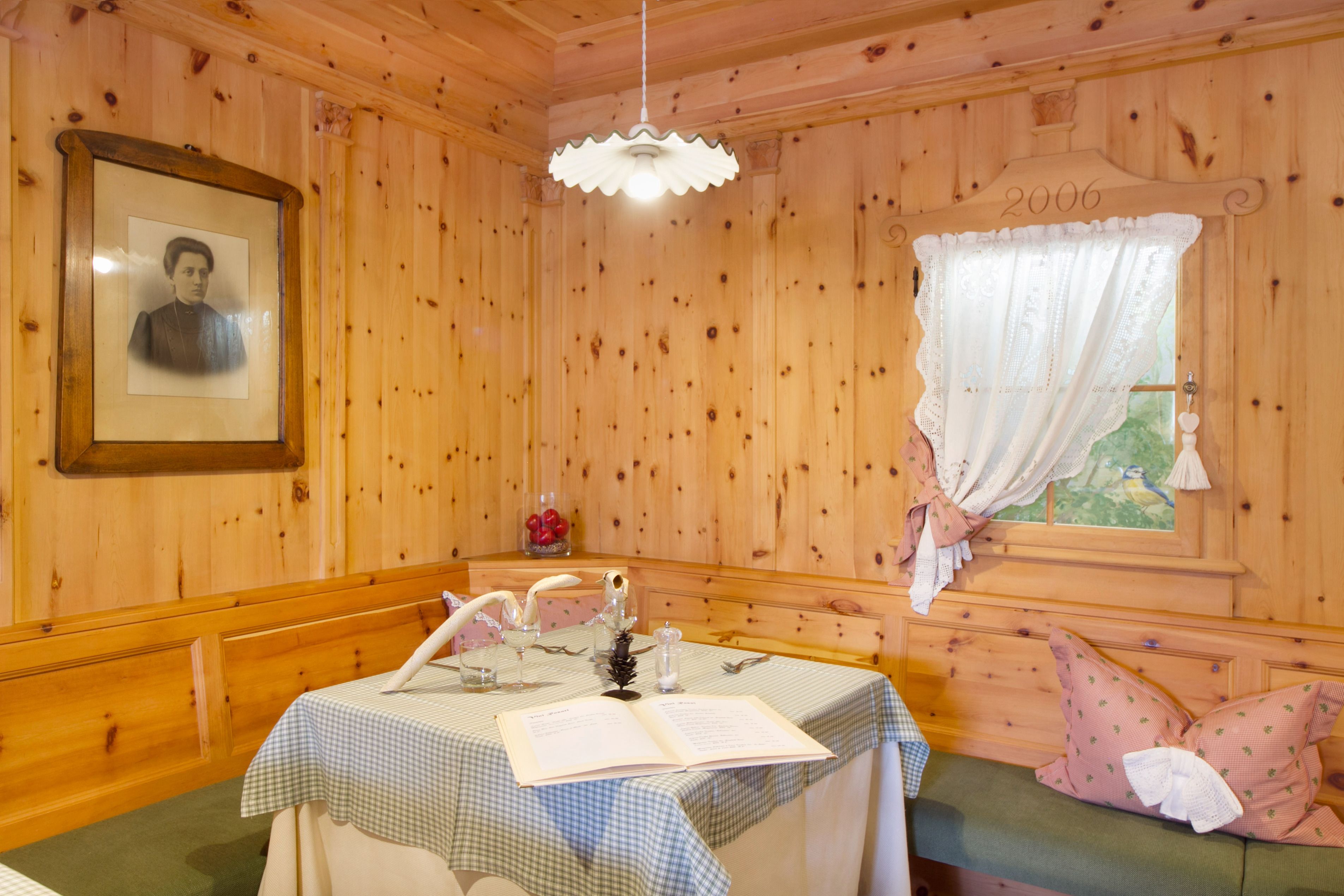 A wooden room with a table set for dining, a framed picture on the wall, and a window with a curtain.