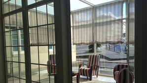 A room with a large glass door leading to an outdoor area with striped chairs and a small table.