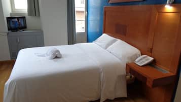 A neatly made bed with white linens, a wooden headboard, a bedside table with a phone, and a TV on a cabinet.