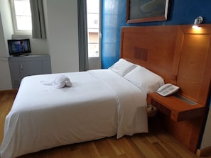 A neatly made bed with white linens, a wooden headboard, a bedside table with a phone, and a TV on a cabinet. - Hotel Villa de Betanzos (Betanzos)