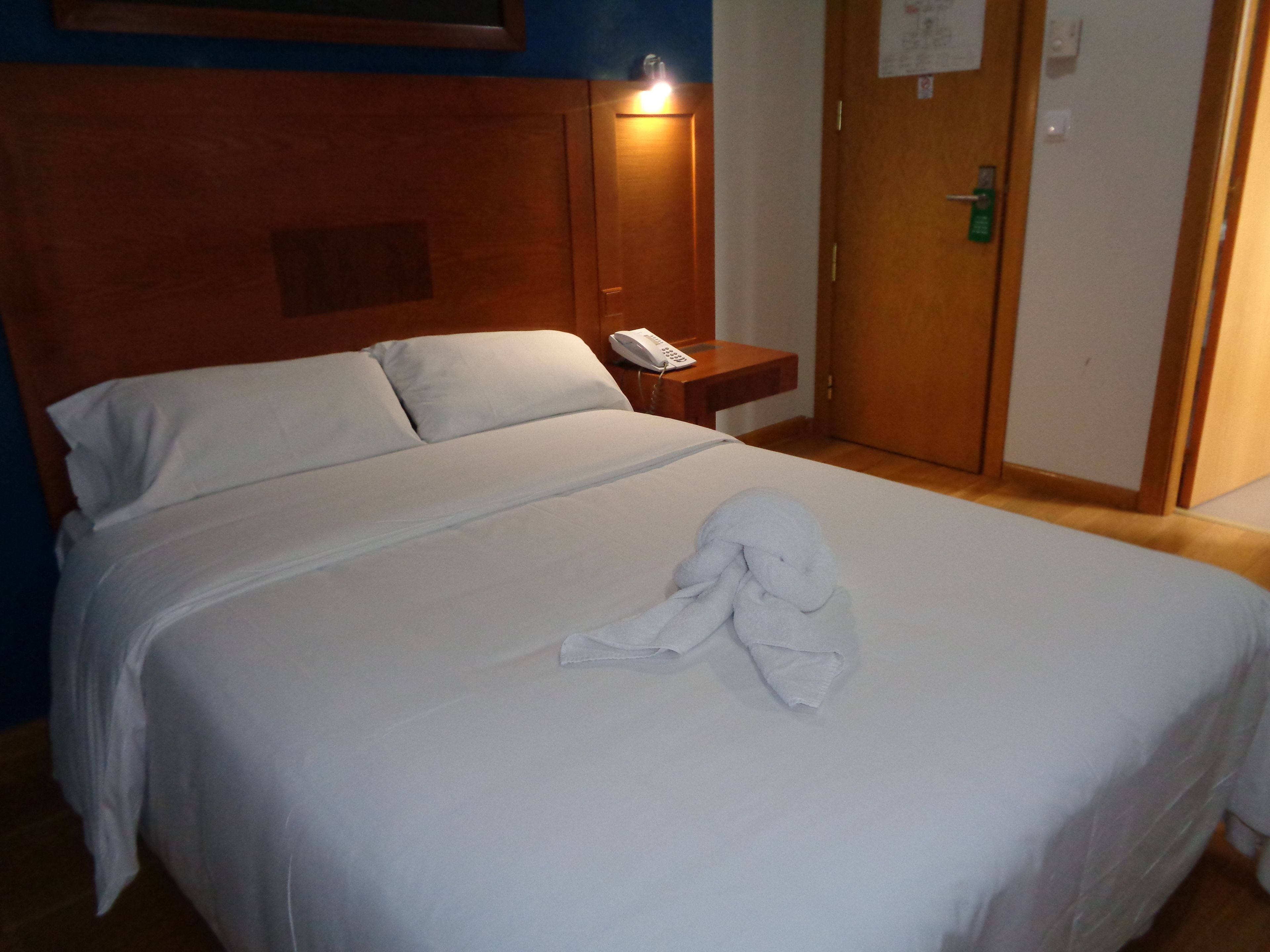 A hotel room with a bed, a bedside table with a phone, and a door with a lock.