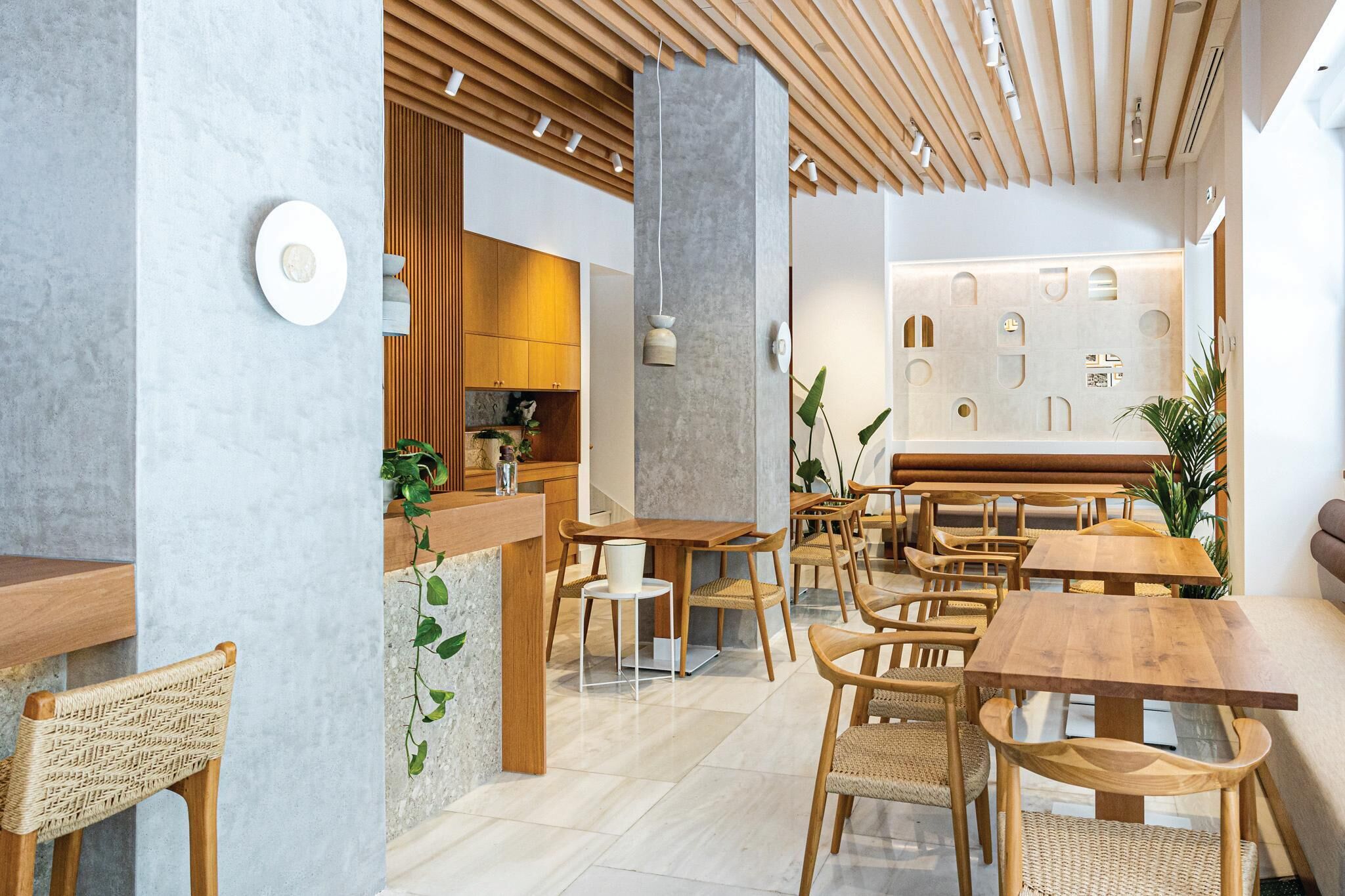 A modern interior with wooden furniture, a central column, and a wall with geometric cutouts.