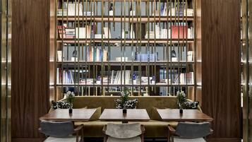 A library with a wooden bookshelf, a sofa, and two tables with chairs.