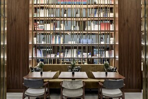 A library with a wooden bookshelf, a sofa, and two tables with chairs.