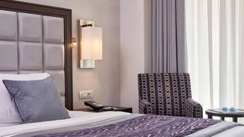 A hotel room with a bed, a nightstand with a phone, a chair, and a window with curtains.