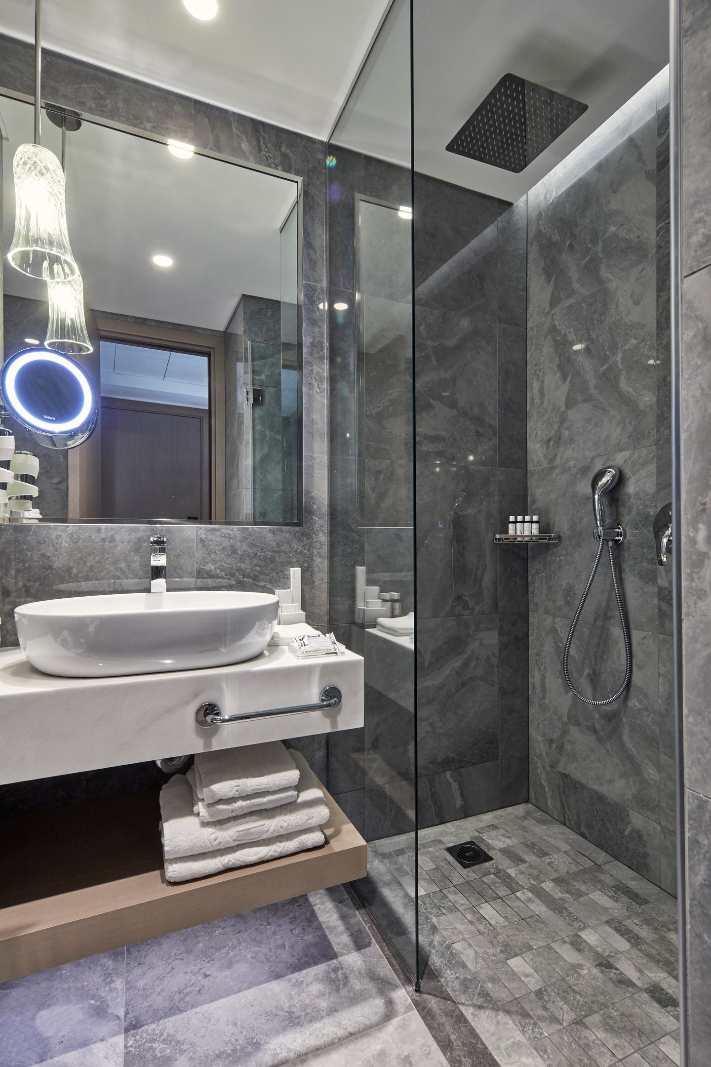 A modern bathroom with a glass shower enclosure, a vanity with a sink, and a mirror with a ring light.