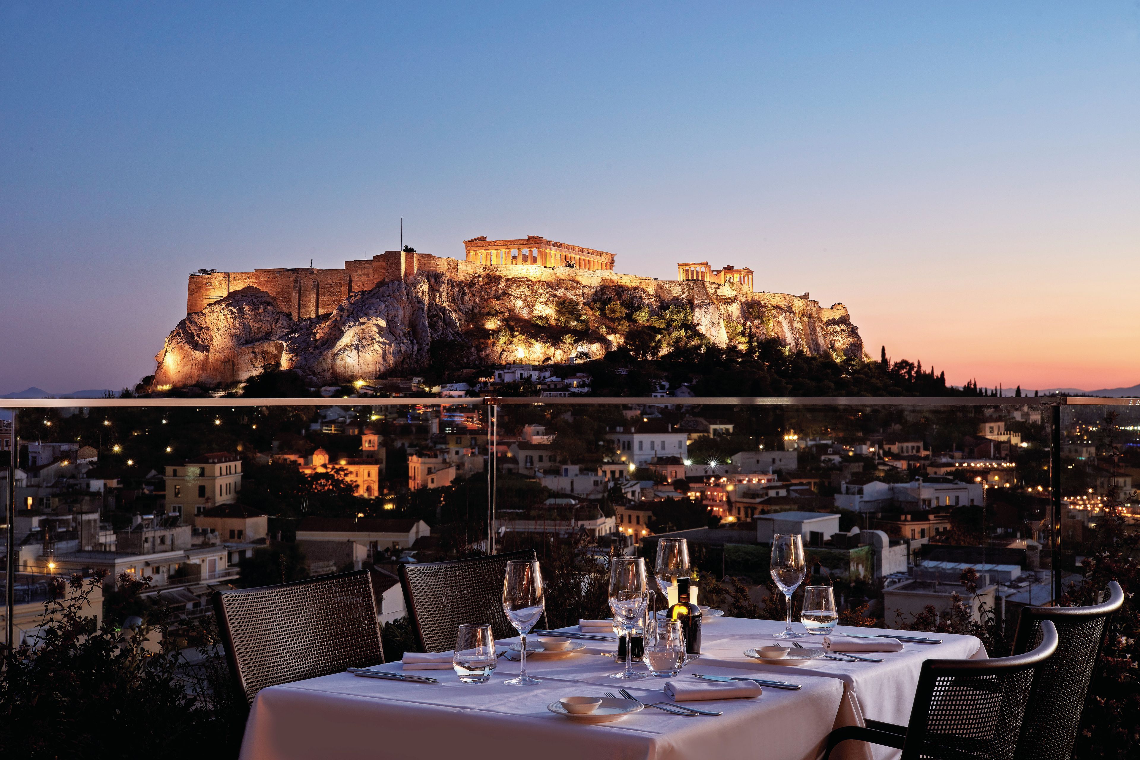A table set for dining with a view of ancient ruins at sunset.