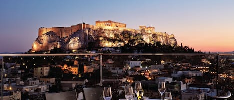 A table set for dining with a view of ancient ruins at sunset.