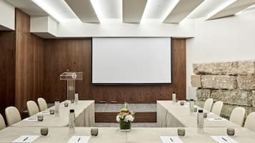 Μια αίθουσα συνεδριάσεων με ένα μεγάλο τραπέζι, καρέκλες, μια οθόνη προβολέα και έναν τοίχο από πέτρα.