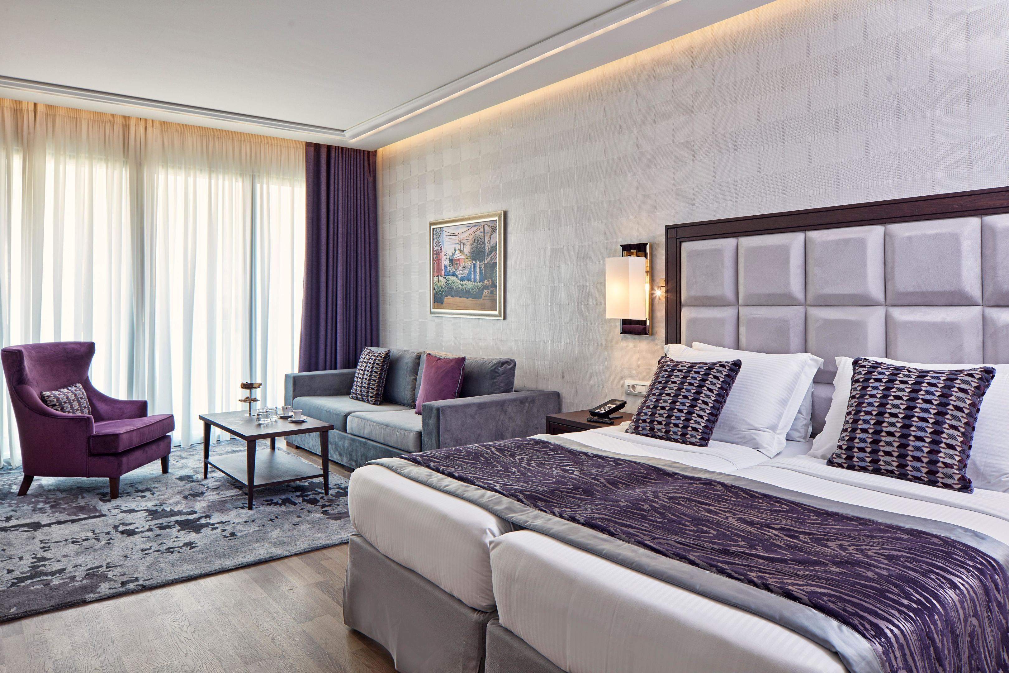 A hotel room with a bed, two armchairs, a small table, and a painting on the wall.