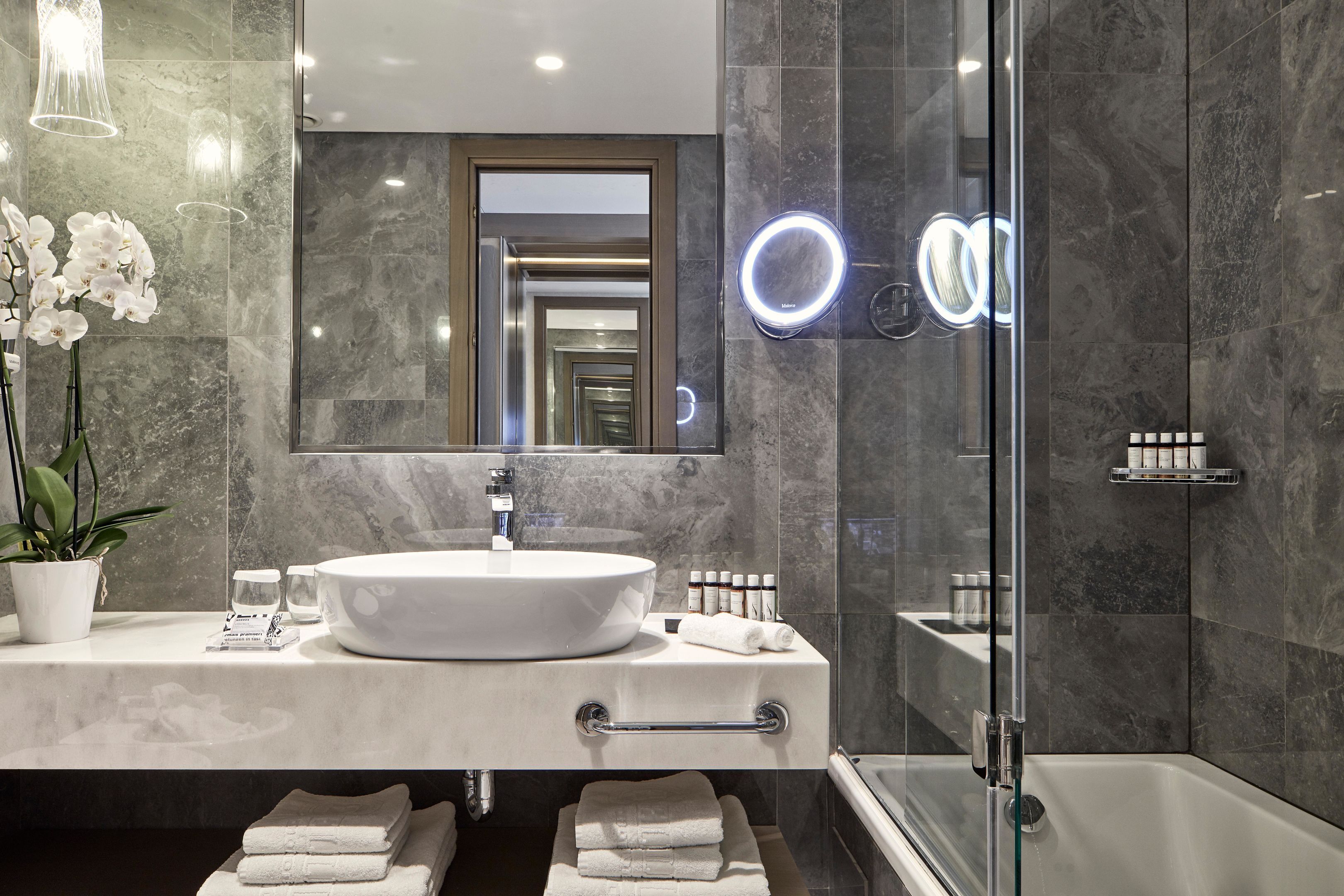 A modern bathroom with a large mirror, a round sink, and a glass shower enclosure.