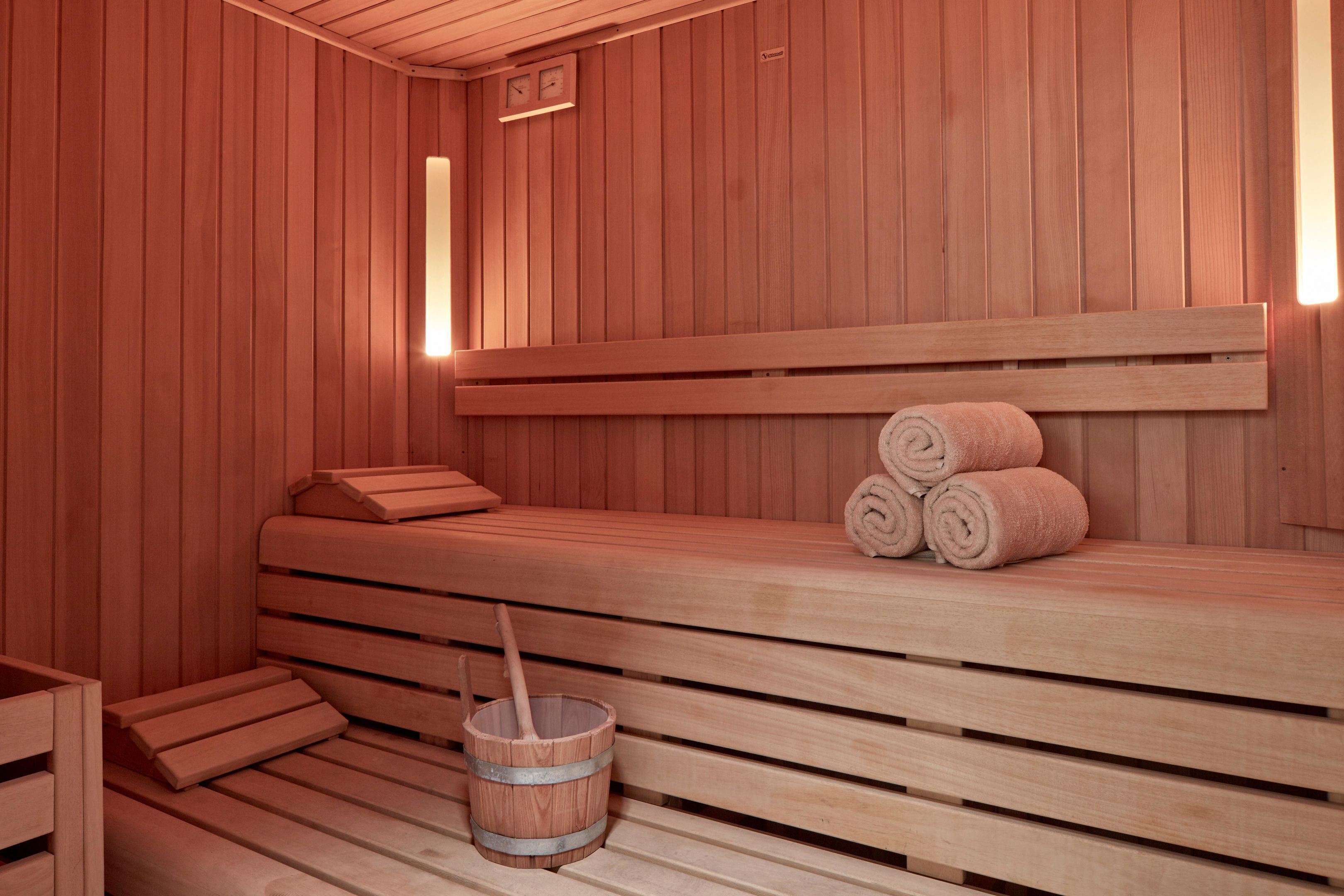 A wooden sauna with benches, a bench with towels, and a wooden bucket.