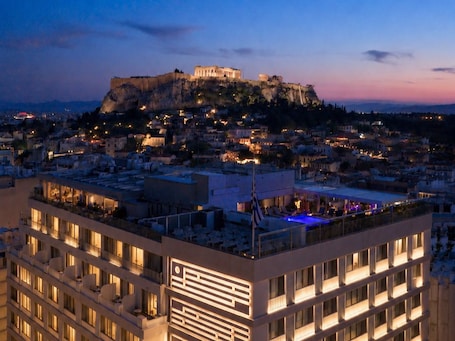A hotel with multiple floors, a rooftop pool with blue lighting, and a view of a historic building on a hill.