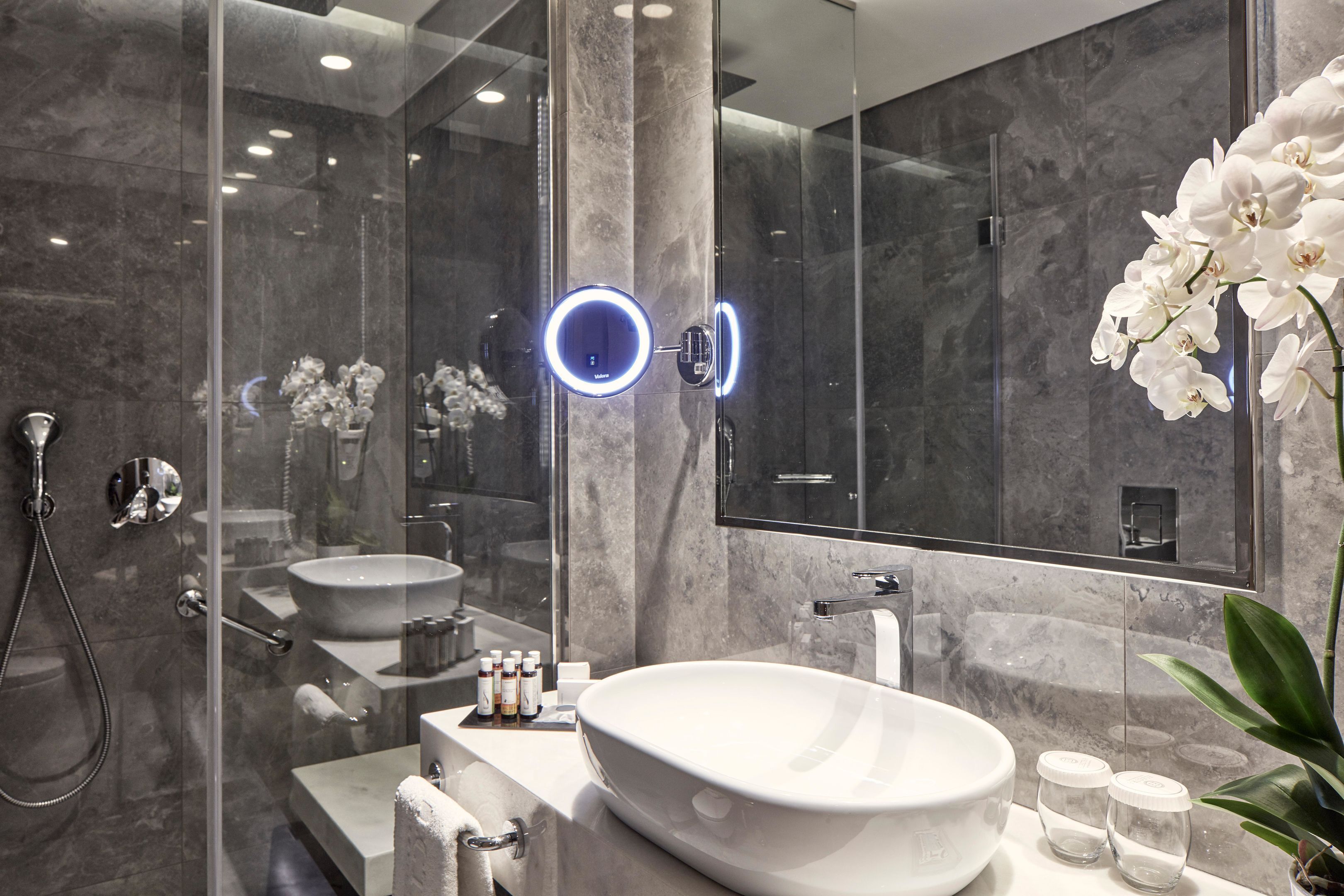 Un baño moderno con un lavamanos ovalado grande, un cabezal de ducha manual y una ducha con cerramiento de vidrio.