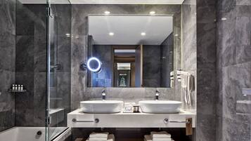 Un baño moderno con dos lavamanos, cabina de ducha con mampara de vidrio y un espejo grande con luz de aro.