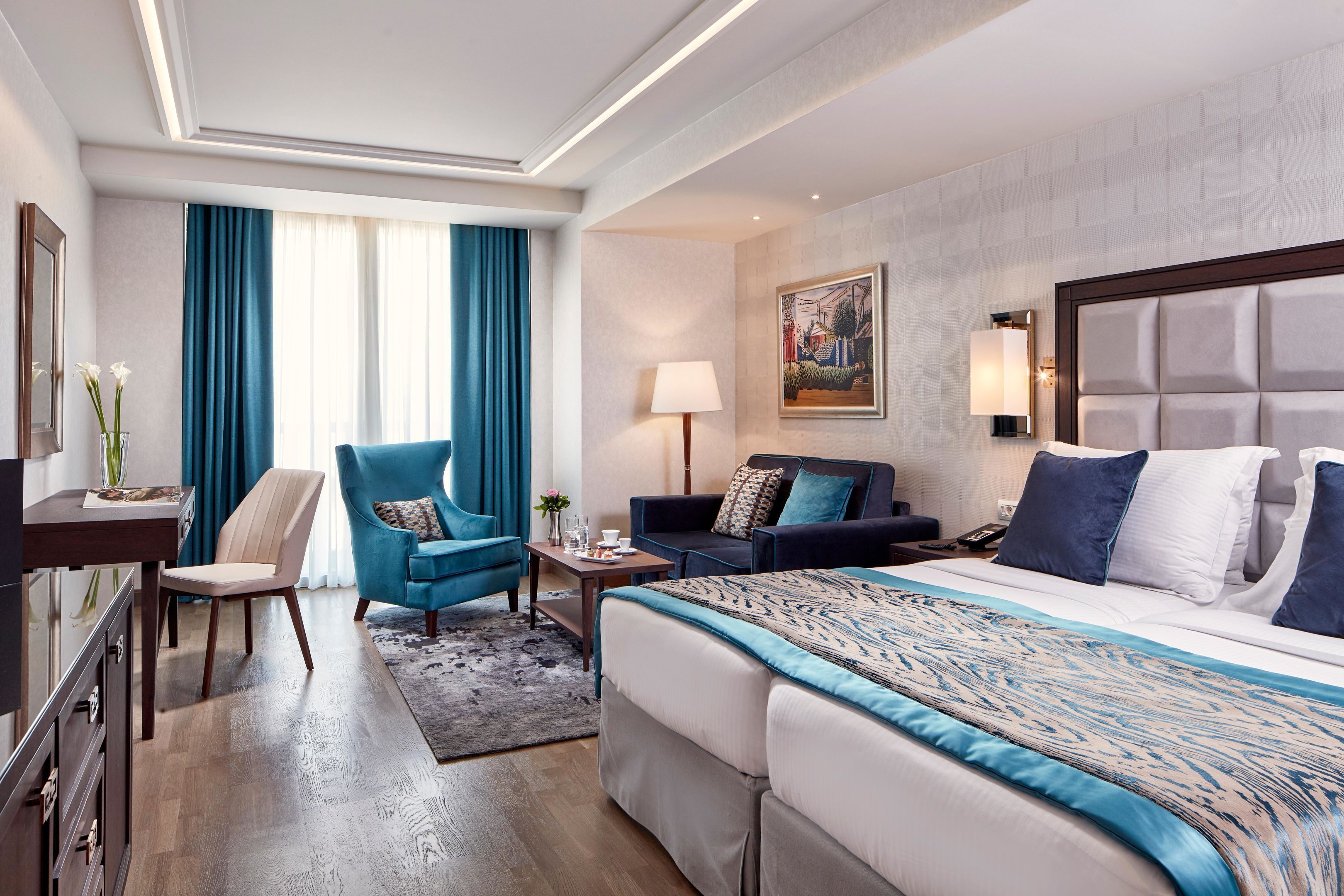 Una habitación de hotel con una cama grande, un escritorio, una silla, un sofá y un cuadro en la pared.