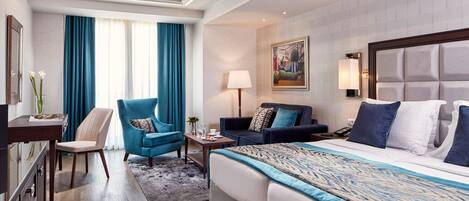 A hotel room with a large bed, a desk, a chair, a sofa, and a painting on the wall.