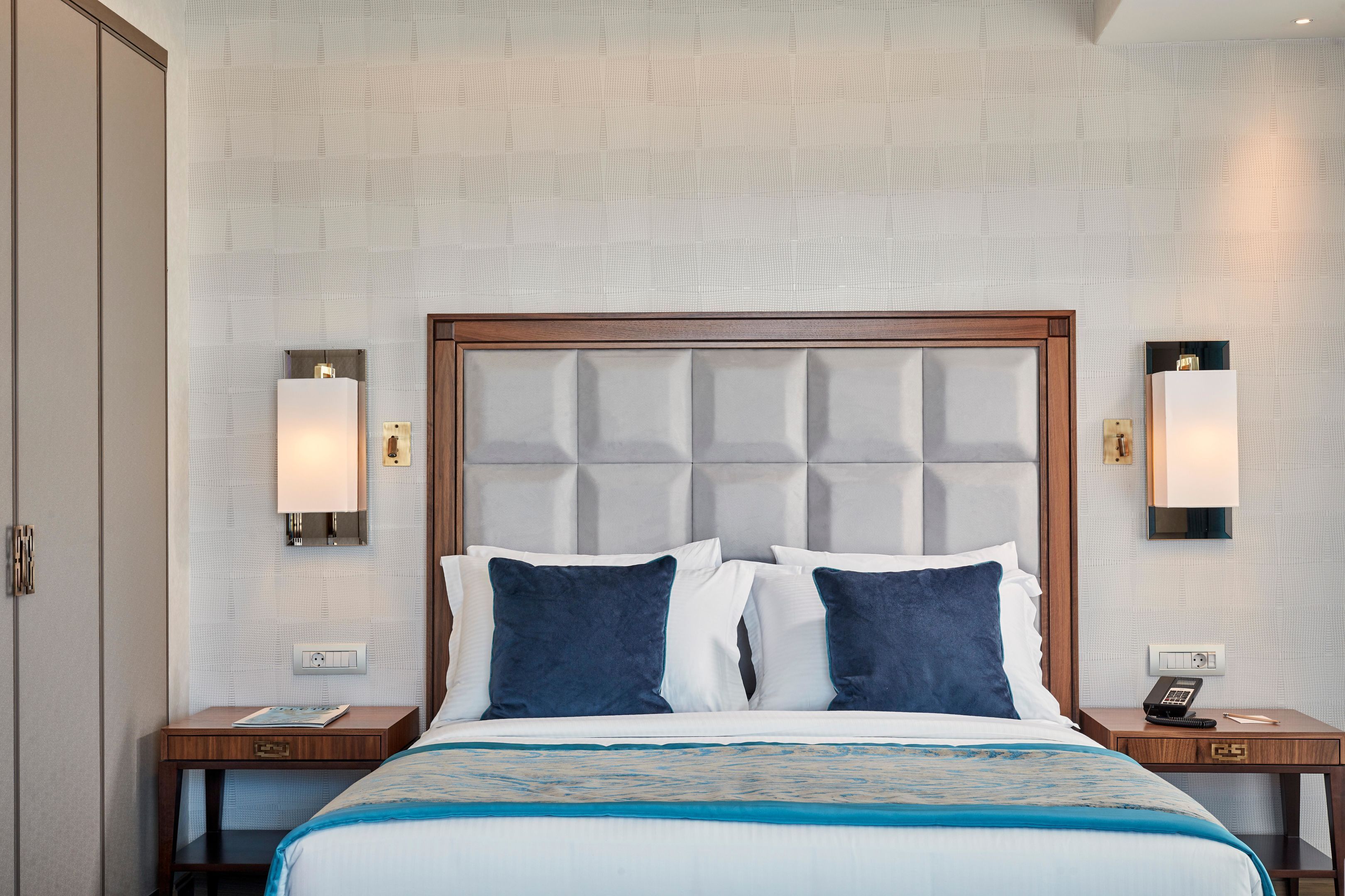 Une chambre d’hôtel avec un grand lit, deux tables de chevet, une tête de lit en bois et des lampes fixées au mur.