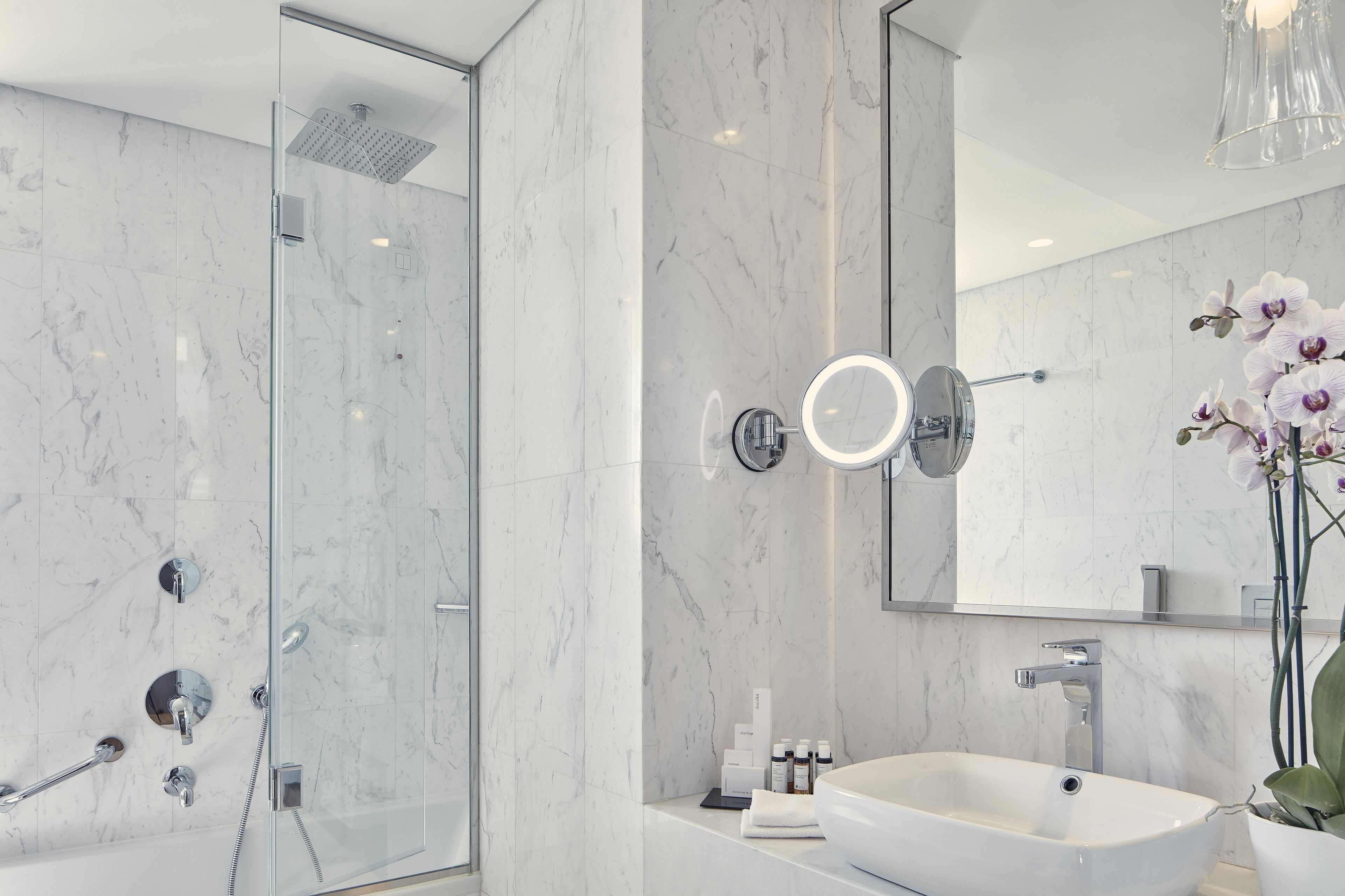 A modern bathroom with a glass-enclosed shower, a white sink, and a large mirror.