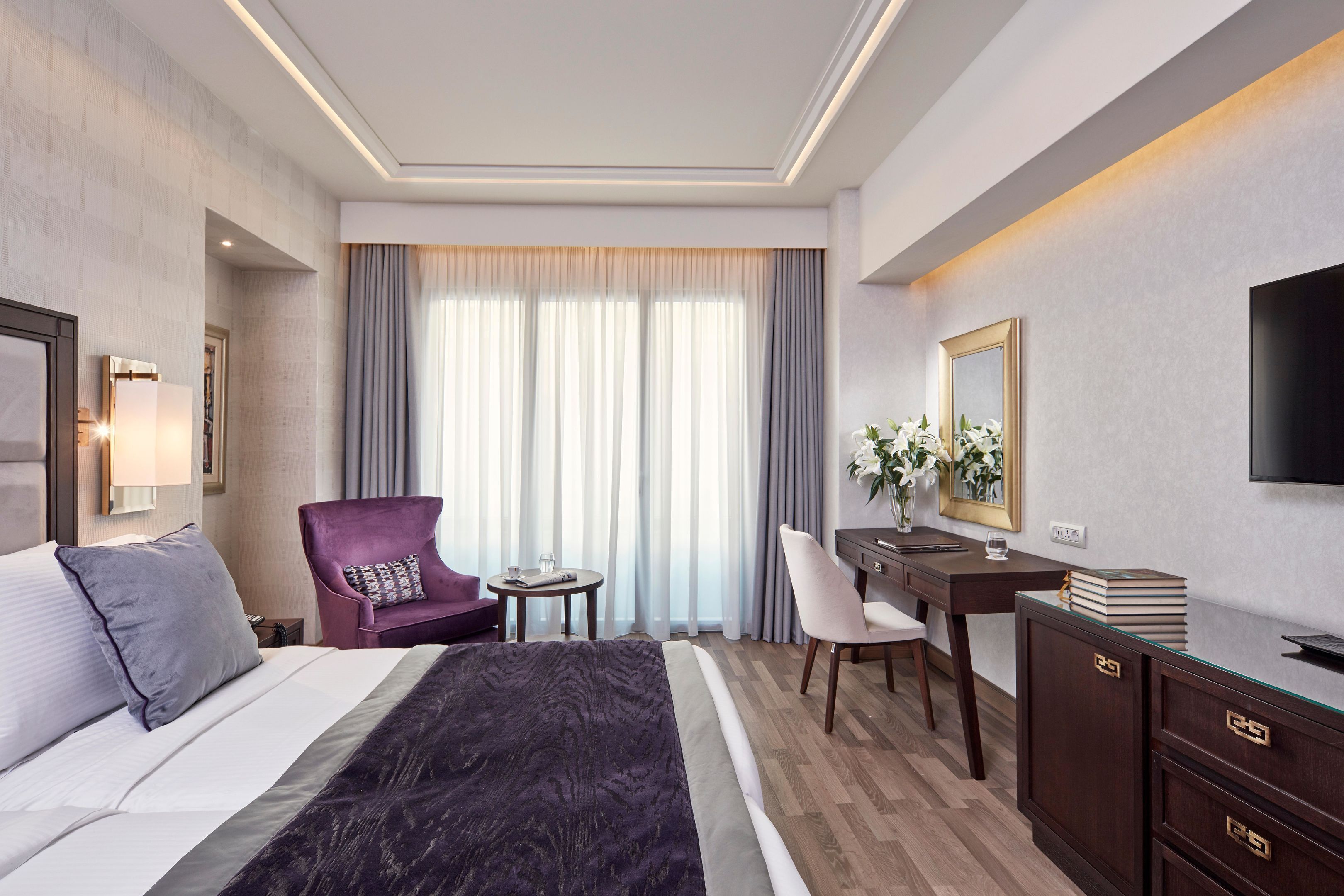 A hotel room with a bed, a desk, a chair, a television, and a window with curtains.