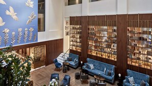 A spacious lobby with a high ceiling, a central staircase, and a seating area with sofas and chairs.