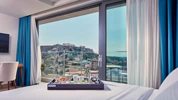 A hotel room with a large window, a bed, a tray with breakfast items, and a view of a cityscape with a historic building.