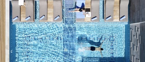 Une piscine où une personne nage, des chaises longues et une terrasse en bois.