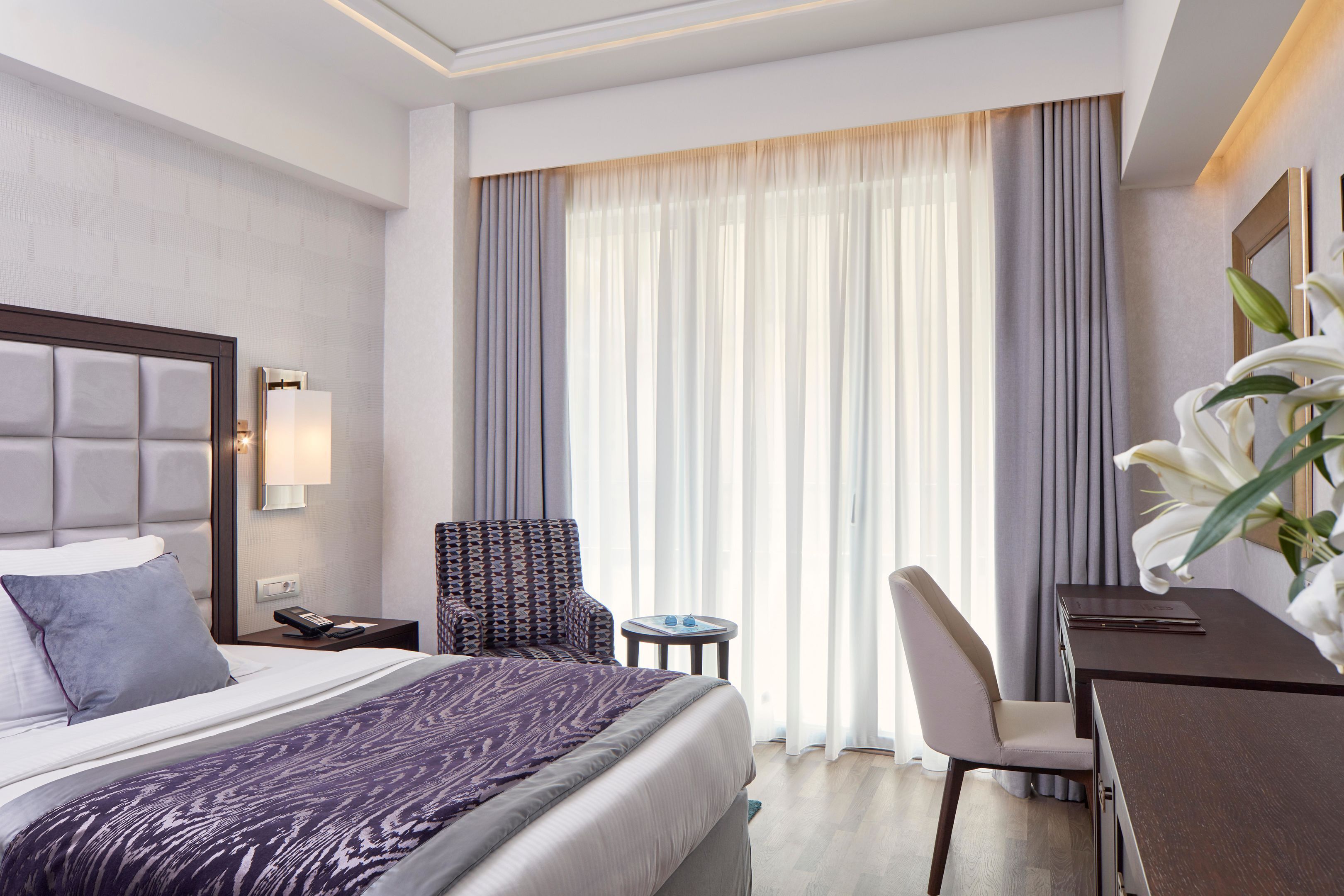 Una habitación de hotel con una cama, una silla, un escritorio y un ventanal con cortinas.