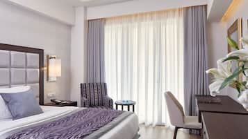 Una habitación de hotel con una cama, una silla, un escritorio y un ventanal con cortinas.
