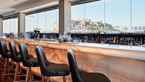 Un bar con mostrador de mármol, taburetes de cuero negro y vistas a un edificio histórico.