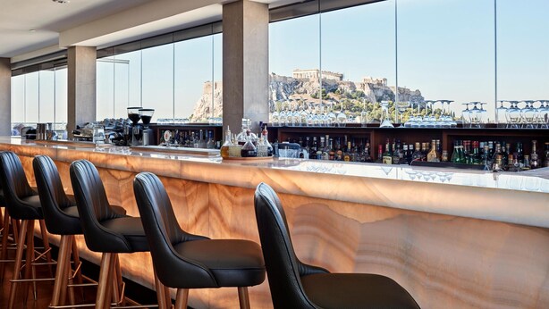 A bar with a marble countertop, black leather bar stools, and a view of a historic building.