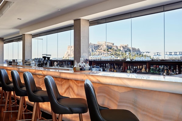 Un bar con mostrador de mármol, taburetes de cuero negro y vistas a un edificio histórico.