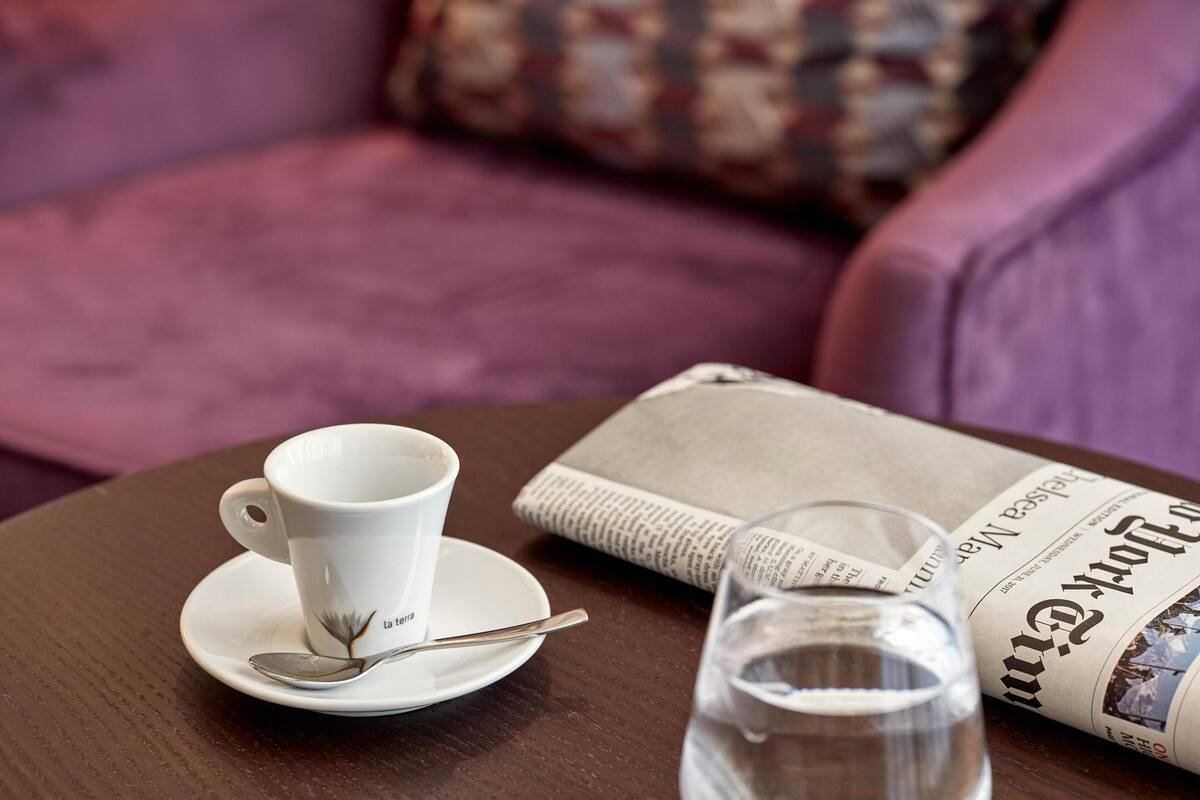 A white cup with a spoon on a saucer, a glass of water, and a newspaper on a table.