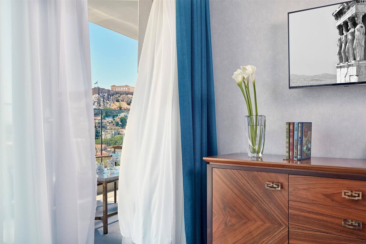 A room with a view of a historic building, a wooden cabinet with books, and a vase with flowers.