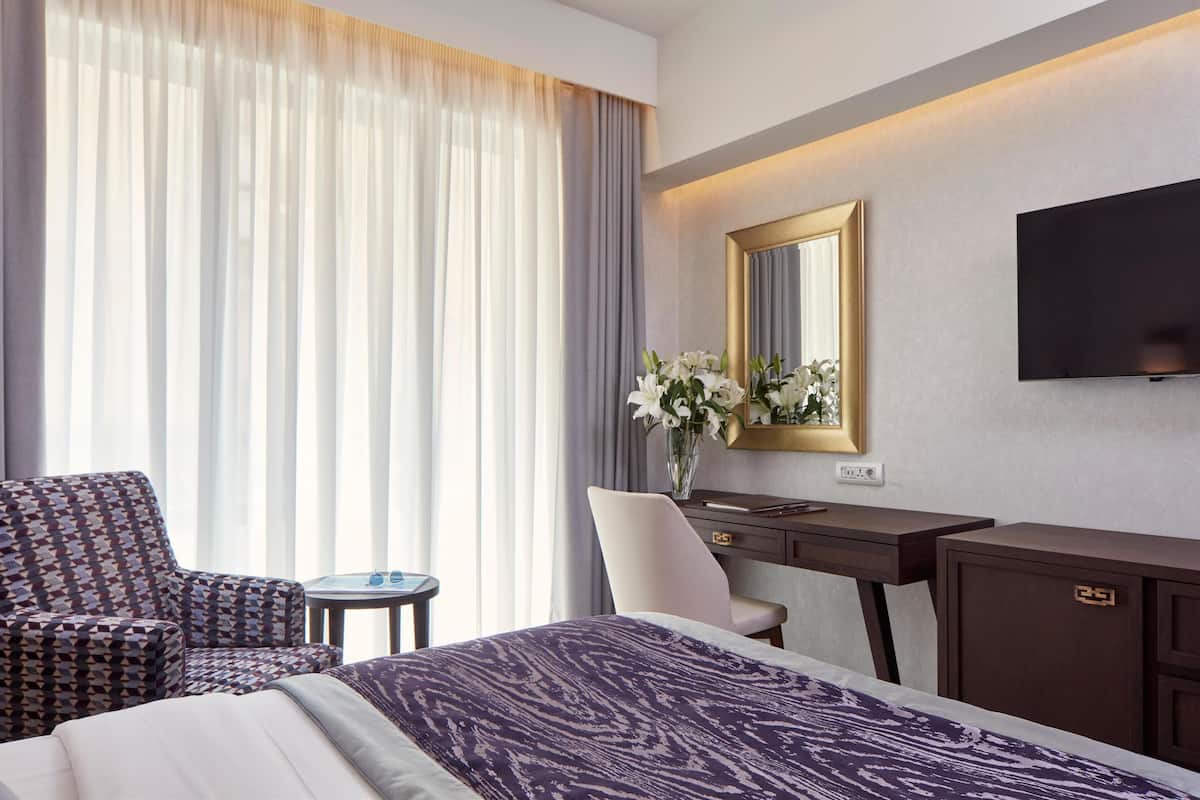 A hotel room with a large bed, a desk, a chair, a TV, and a window with curtains.