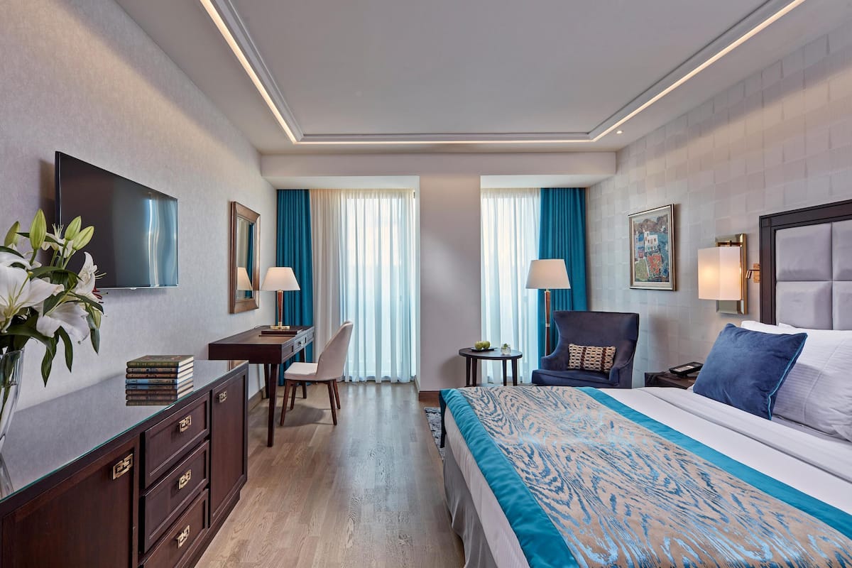 A hotel room with a bed, desk, chair, and a TV on the wall.
