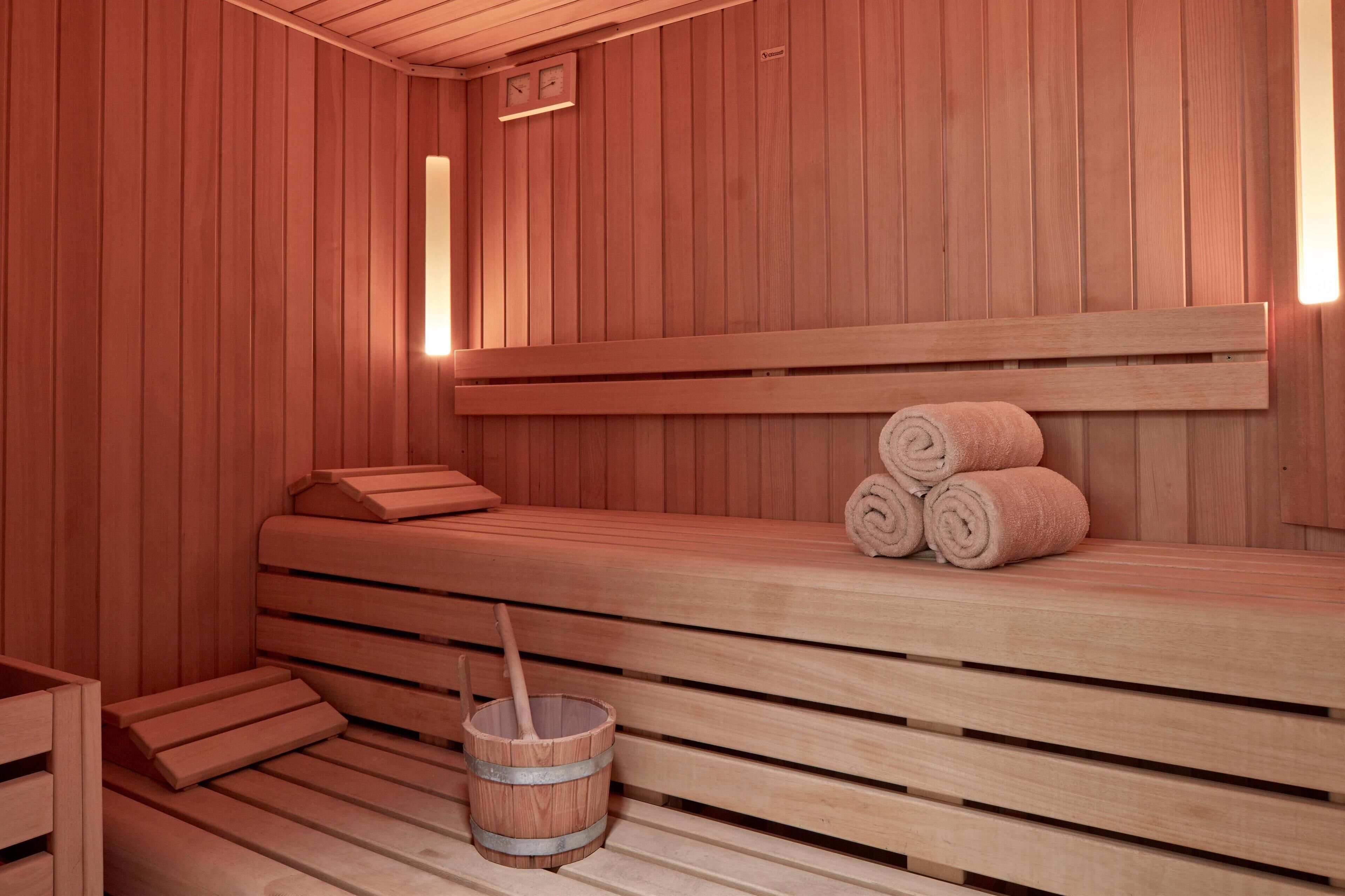 Una sauna de madera con bancos, un asiento en banco y un cubo de madera.