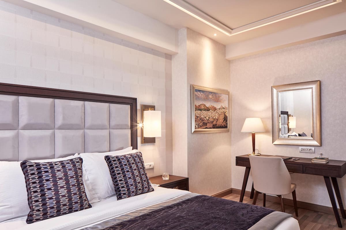 A hotel room with a large bed, a desk, a chair, and a painting on the wall.
