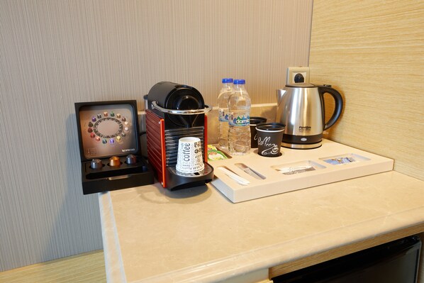 A coffee station with a coffee machine, water bottles, a cup, and a tray with coffee pods. - Park Dedeman Bostanci Hotel (Istanbul)