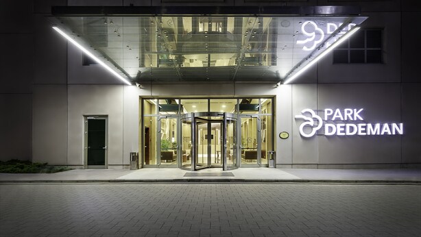Entrada de hotel con puerta giratoria, fachada de vidrio y señalización iluminada.