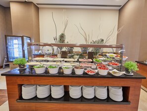 Mesa de buffet con distintos alimentos y un refrigerador al fondo.