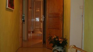 Un pasillo con una puerta de madera, una puerta blanca y un jarrón con flores.