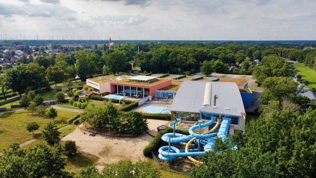 Un resort con un amplio área de piscina, un tobogán acuático y un edificio con techo verde.