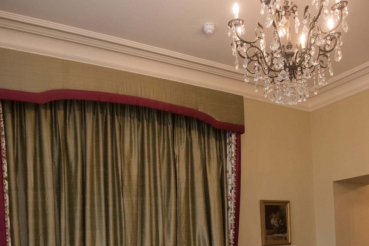 A hotel room with a large bed, a chandelier, a red chair, and a painting on the wall.