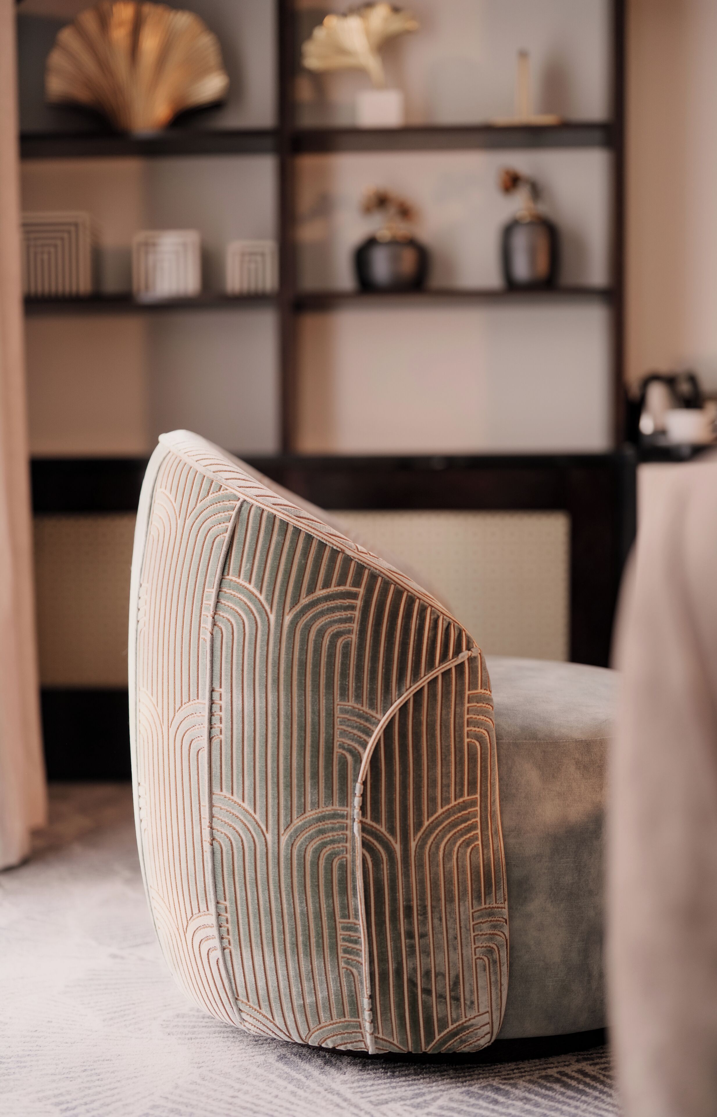 Un rincón de una habitación con un cojín estampado sobre un sofá gris, un estante con objetos decorativos y una alfombra con diseño.